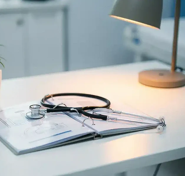 Open noodrespons-binder op een klinisch bureau met een stethoscoop, potplant en bureaulamp in koele blauwtinten.